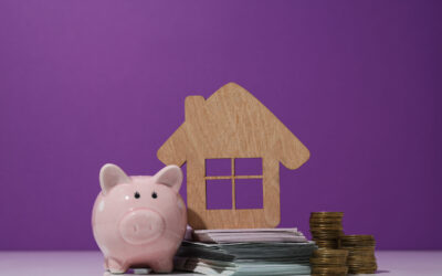 Wooden house, money, and piggy bank on purple background